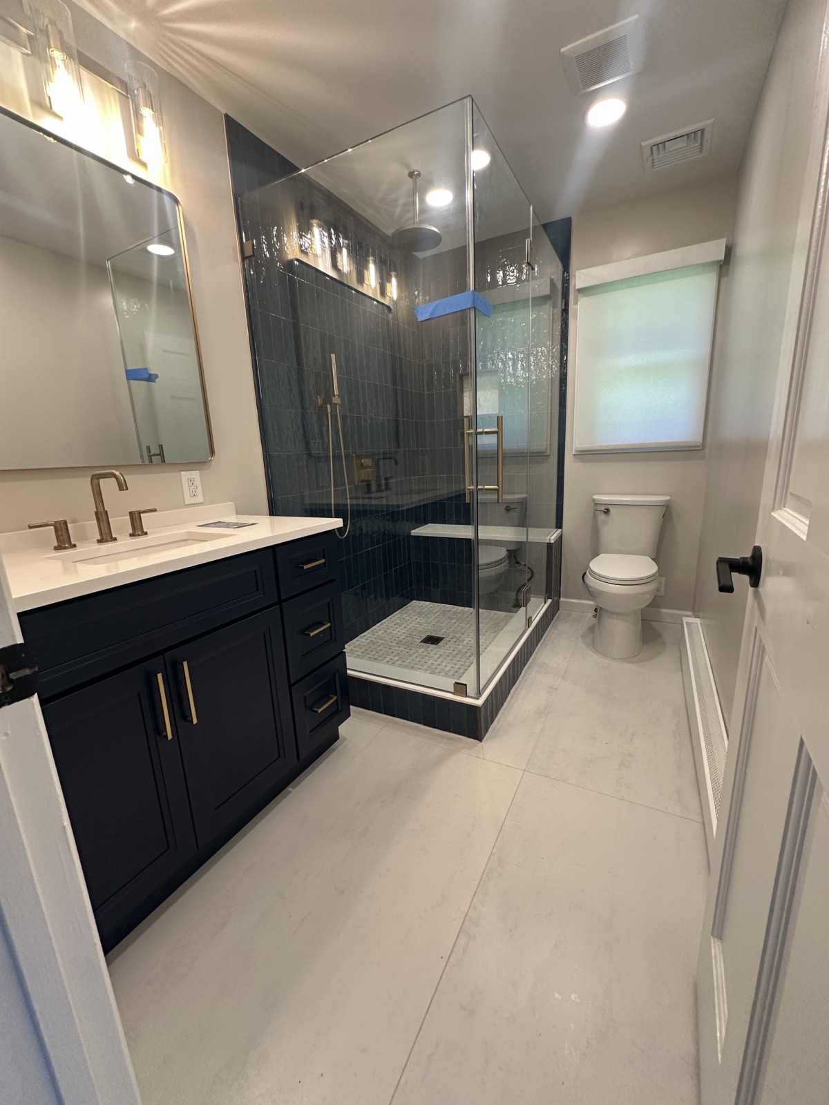 Navy and white bathroom remodel with walk-in glass shower and gold fixtures