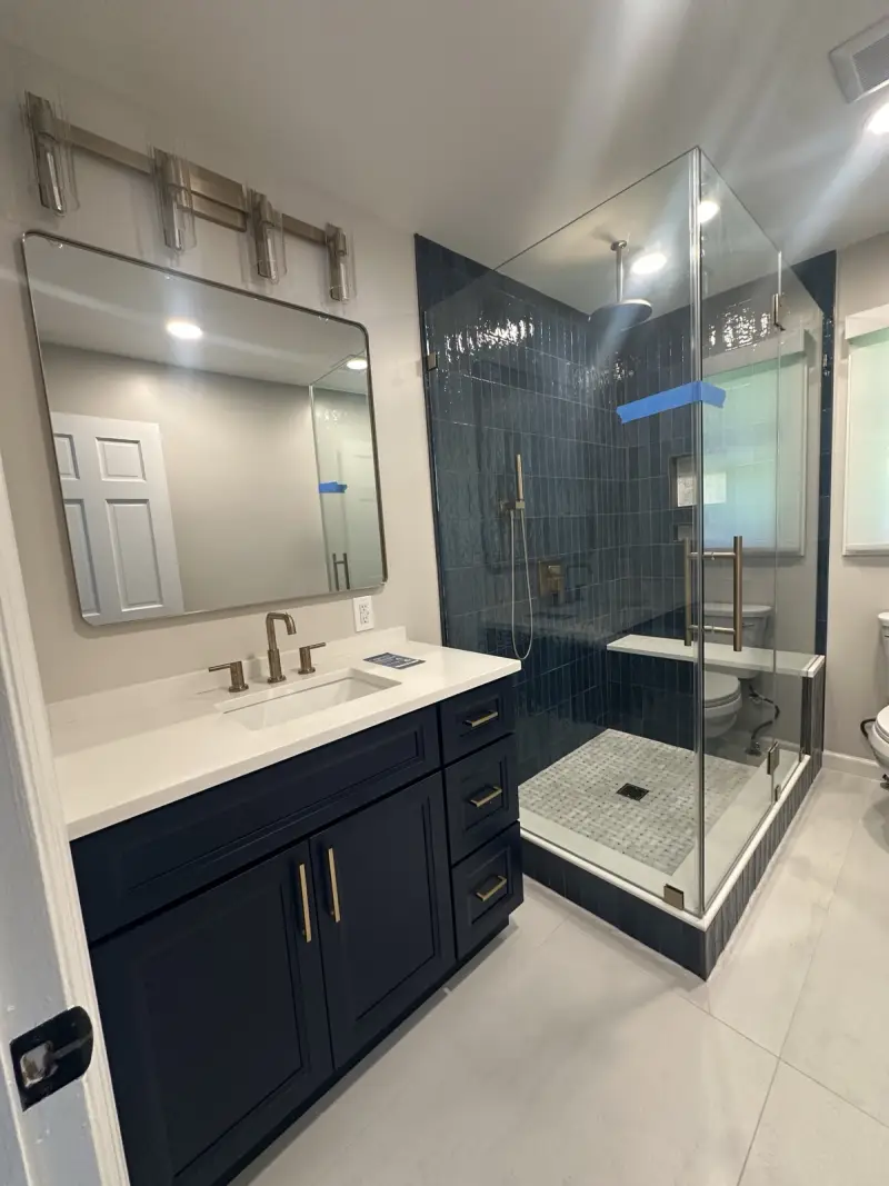 Modern bathroom remodel with navy tile shower, glass enclosure, and gold fixtures